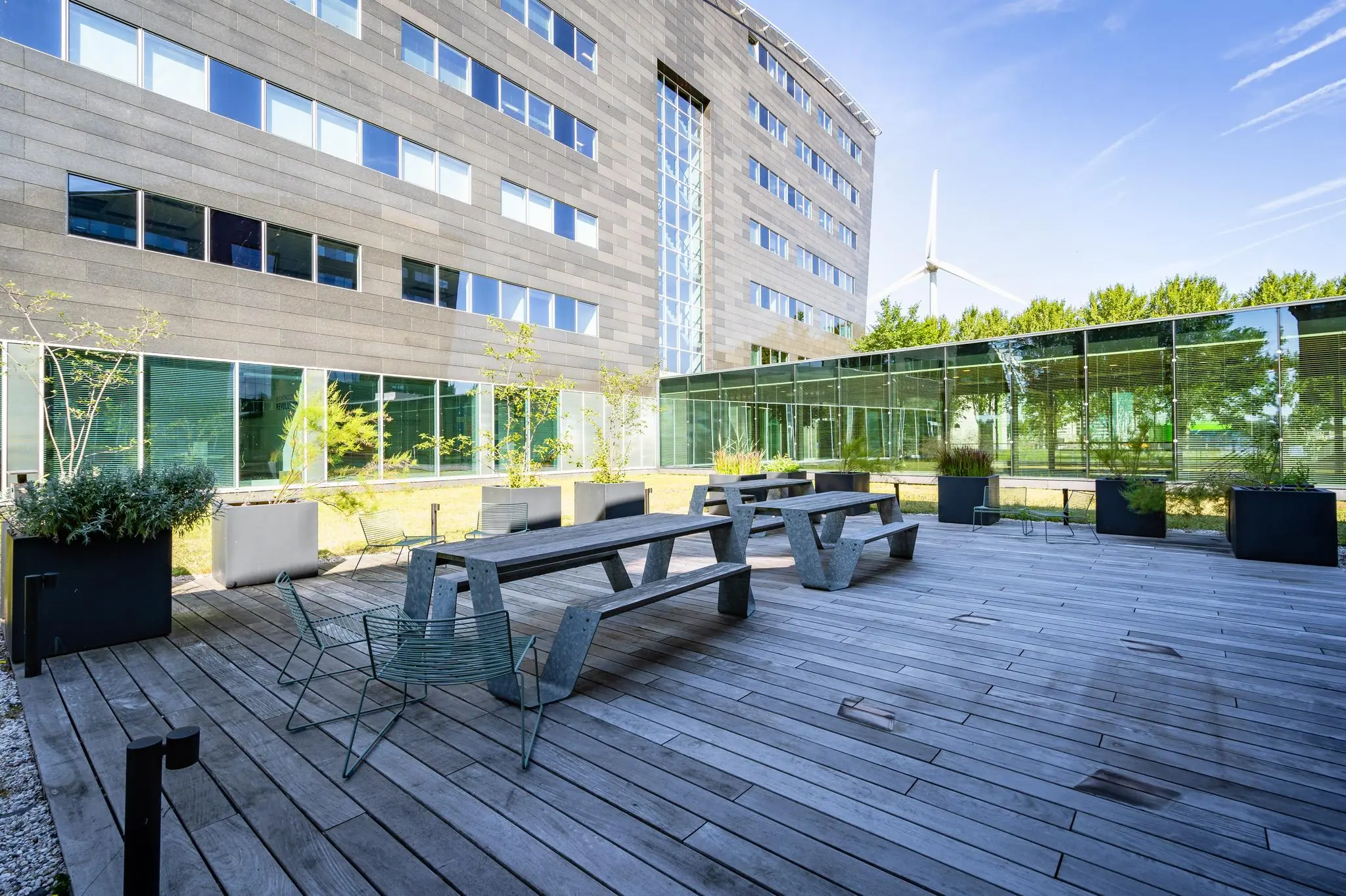 Moderne kantooromgeving aan de Rivium Promenade met houten terras, zitbanken en groenvoorziening.